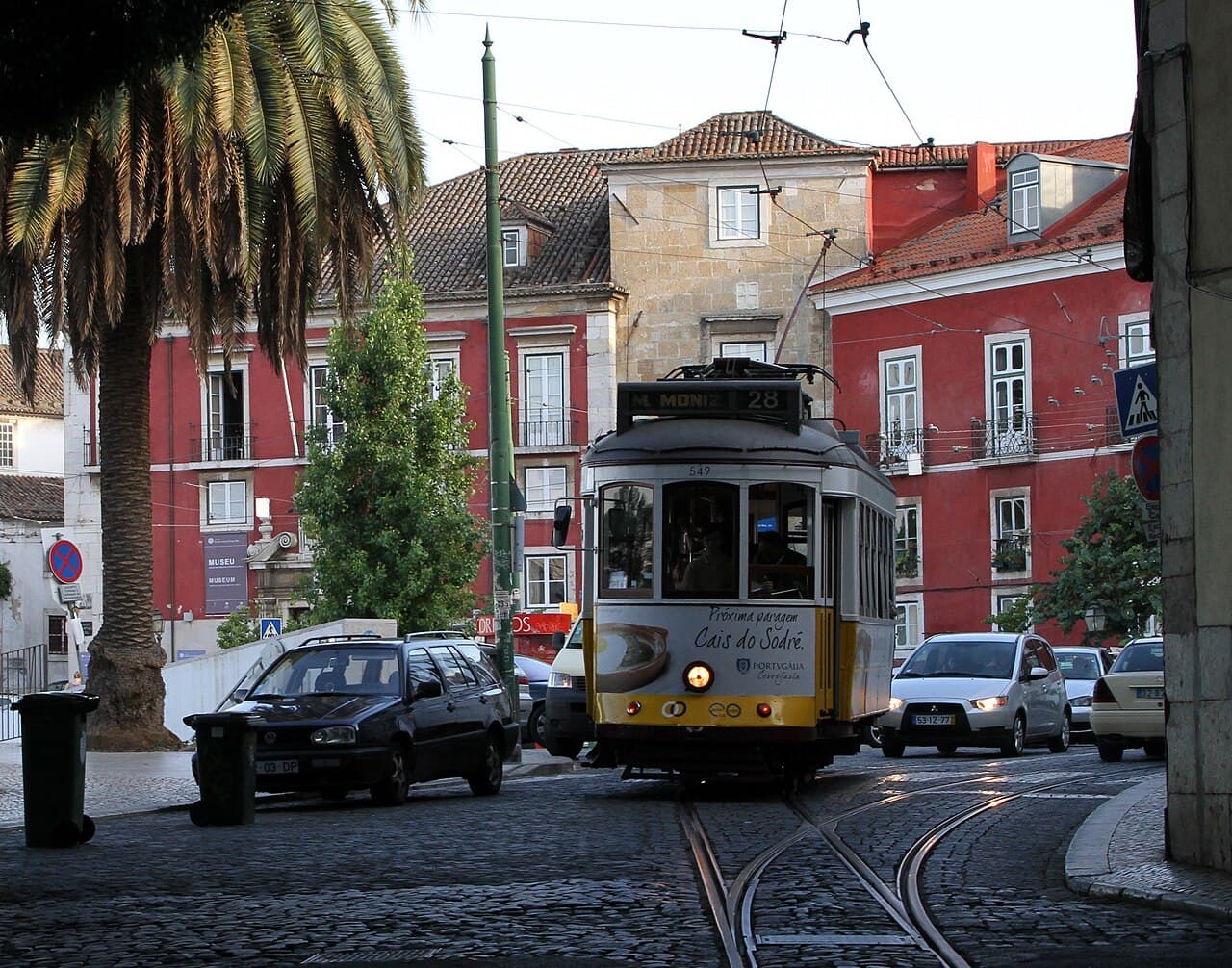 A yellow route-28 tram on a cobbled Alfama street in Lisbon, near the riverside Santa Apolonia club district